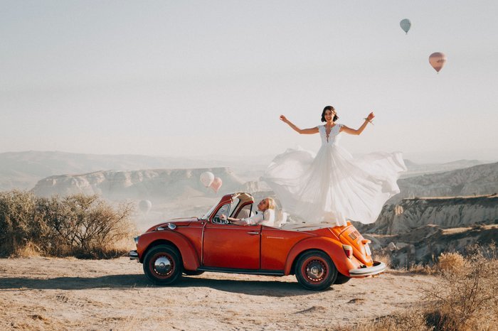 Веселый свадебный портрет невесты, стоящей на заднем сиденье автомобиля в пустыне
