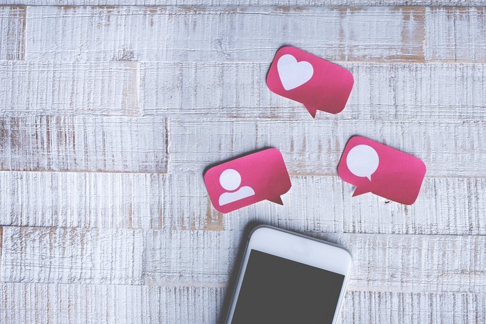 Смартфон с розовыми бумажными иконками социальных акций и лайков над ним