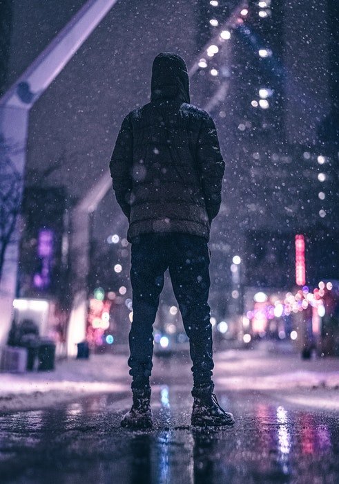 Мужчина в зимней одежде стоит на городской улице во время снегопада