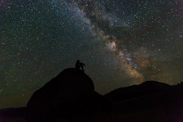Потрясающий астрофотографический снимок силуэта человека на скале на фоне усыпанного звездами неба