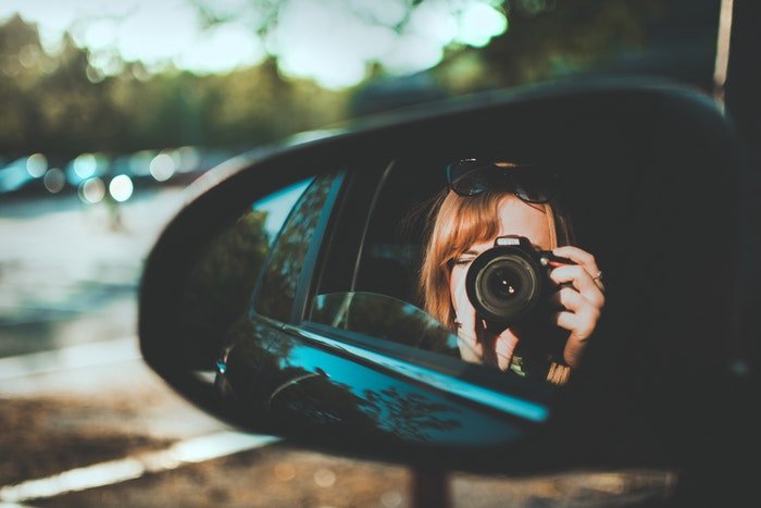 Девушка делает селфи с зеркальным фотоаппаратом из бокового зеркала автомобиля