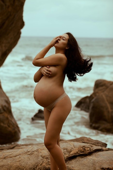 Красивое будуарное фото беременной женщины, позирующей обнаженной на пляже
