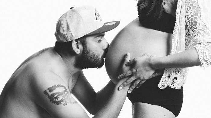 Черно-белая будуарная фотография мужчины, целующего живот своей беременной жены