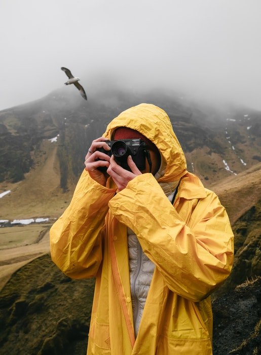 фотограф в желтом снимает в дождливый день в горах с птицей за спиной