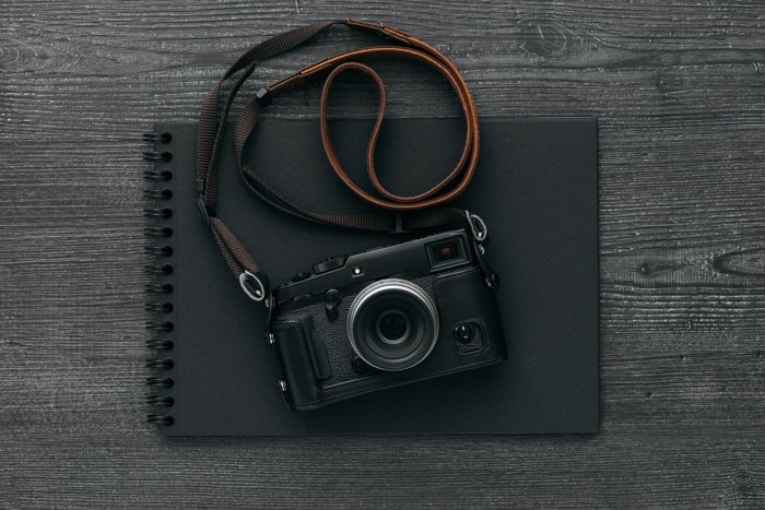 Пустой черный фотоальбом и профессиональный цифровой фотоаппарат с кожаным ремешком на темном рабочем столе