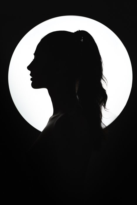 Изобразительный силуэт молодой женщины на фоне круглого источника света. 