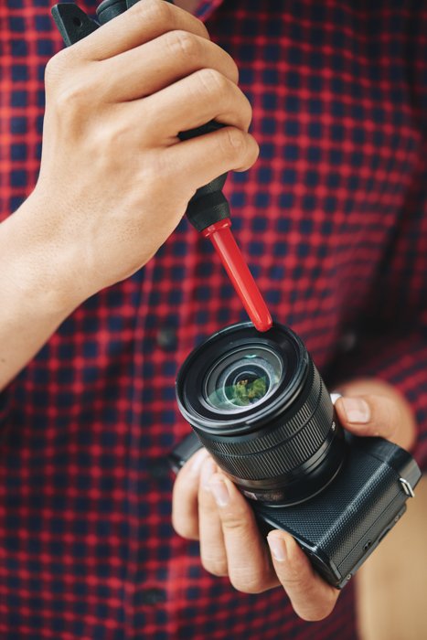 Мужчина чистит объектив своей камеры с помощью черно-красной воздуходувки и раствора для чистки линз. 