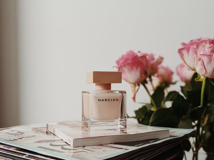Product photo of perfume on the desk beside pink roses