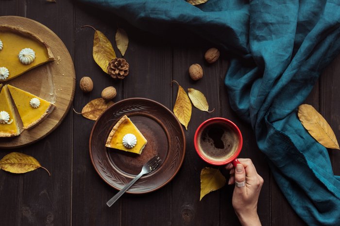 Тыквенный пирог и горячий напиток на столе с осенними листьями, грецкими орехами и кедровыми шишками