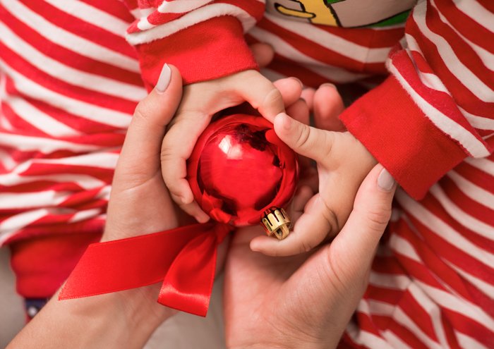 Close up of the couple holding their babies hands with a Christmas decoration