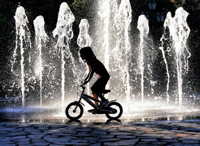 изображение ребенка, катающегося на велосипеде перед фонтаном с подсветкой