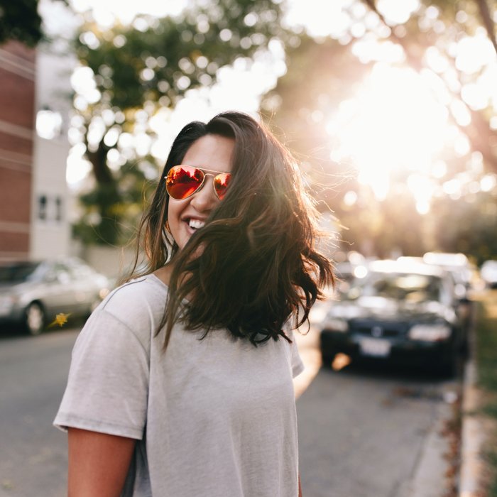 изображение женщины в солнцезащитных очках на городской улице с подсветкой закатного солнца