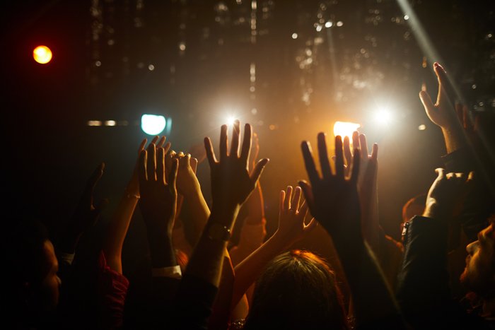 Толпа людей стоит в темном клубе и машет руками в воздухе