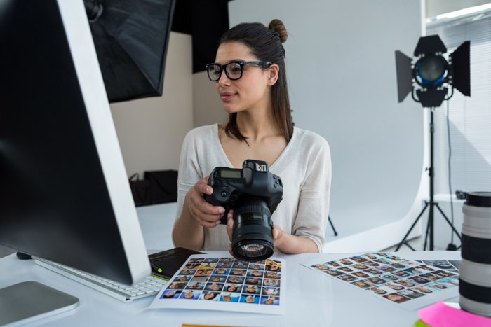 женщина-фотограф держит камеру, глядя на экран своего компьютера в студии