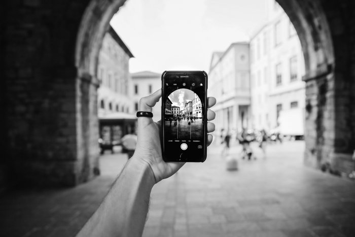 черно-белое изображение руки, держащей смартфон в переулке