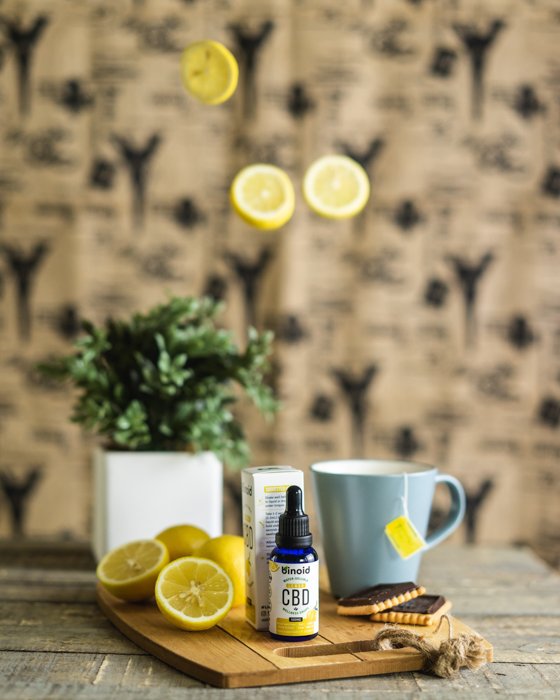 Product photography lifestyle image of the CBD bottle on a dining room table and lemons suspended in the air