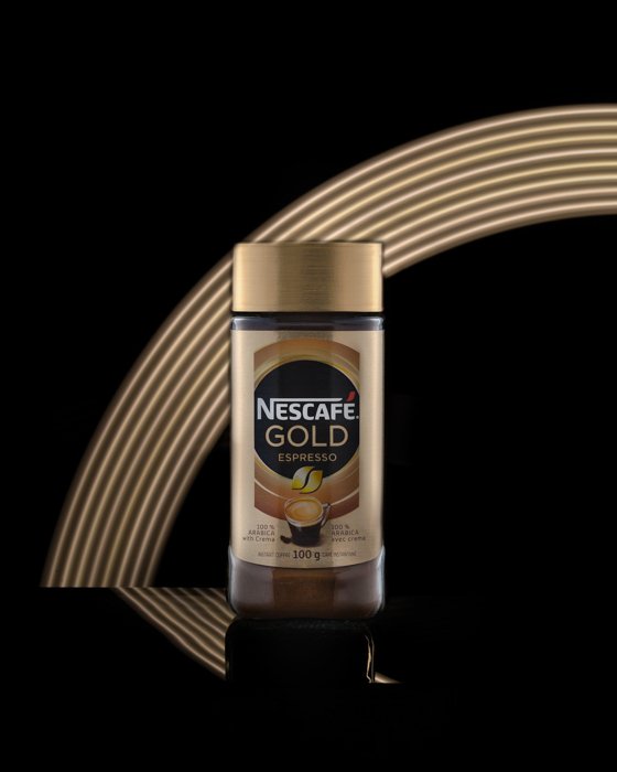 Product photography image of a Nescafe bottle shot in a studio with a gold rainbow in the background