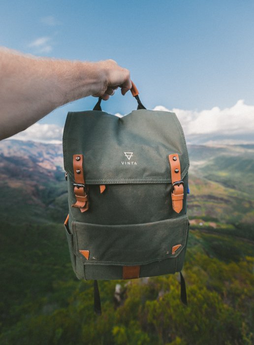 Фотография продукта, изображающая рюкзак на фоне размытого природного пейзажа неба, холмов и леса