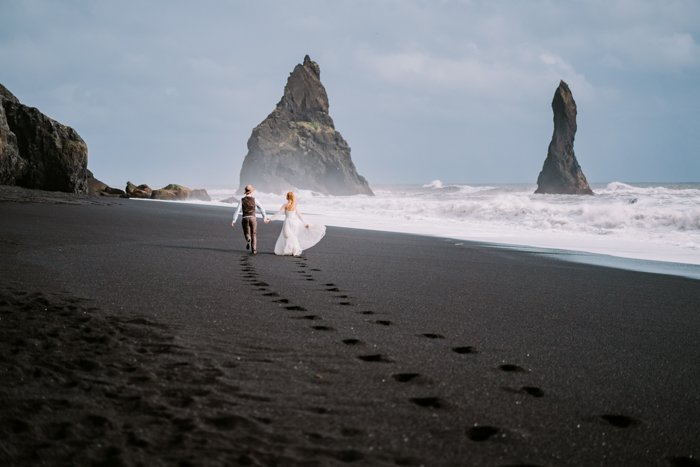 изображение супружеской пары, идущей рука об руку по пляжу с черным песком