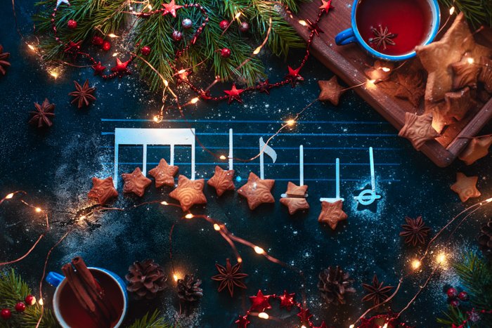 Ноты рождественской мелодии на плоском плане с печеньем в форме звезды, еловыми ветками, деревянным подносом, звездочками аниса и украшениями.