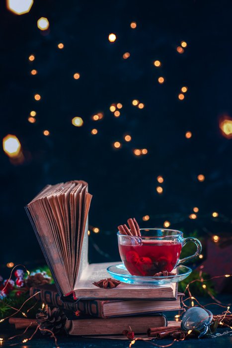 Redberry tea on a stack of books with fairy lights. Рождественский напиток на темном фоне с пробелами