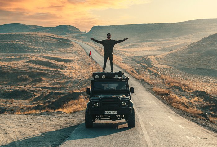 приключенческая фотография человека, стоящего на вершине грузовика во время езды по пустыне