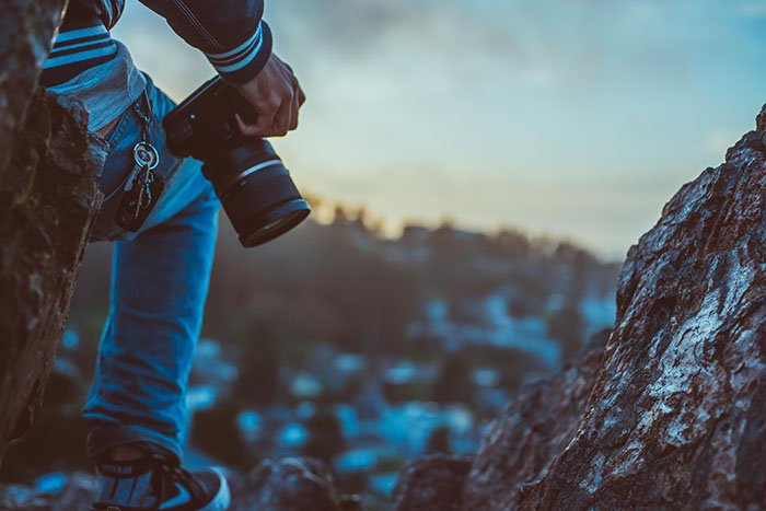 изображение крупным планом человека с фотоаппаратом в руках, опирающегося на скалу