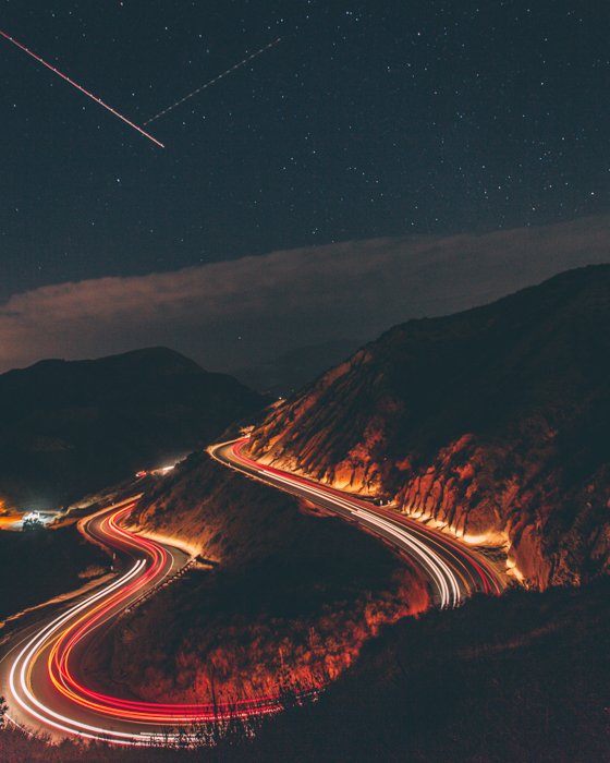 time lapse фото автомобилей, едущих по извилистой горной дороге с падающими звездами на небе