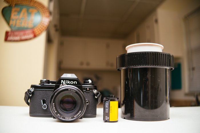 изображение пленочной камеры Nikon, катушки с пленкой и бачка с проявителем на столе