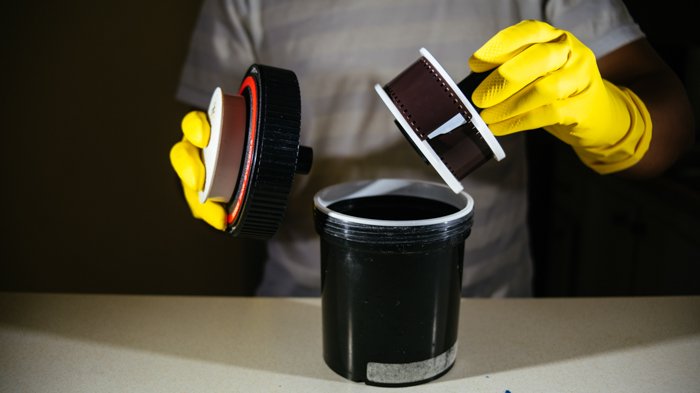изображение человека в желтых перчатках, использующего бак для проявки пленки