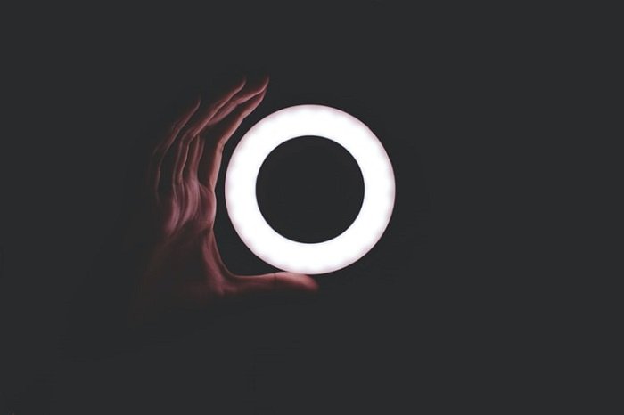Кольцо-светильник натурального цвета на темном фоне с изогнутой вокруг него рукой