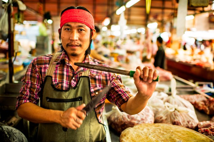 Экологическая портретная фотография рыночного мясника, держащего ножи вверх ногами в Таиланде