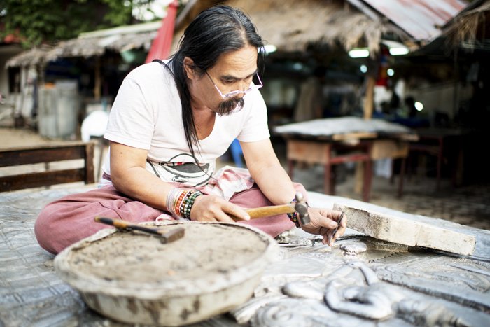 Мужчина работает с молотком в мастерской художника на открытом воздухе в Таиланде