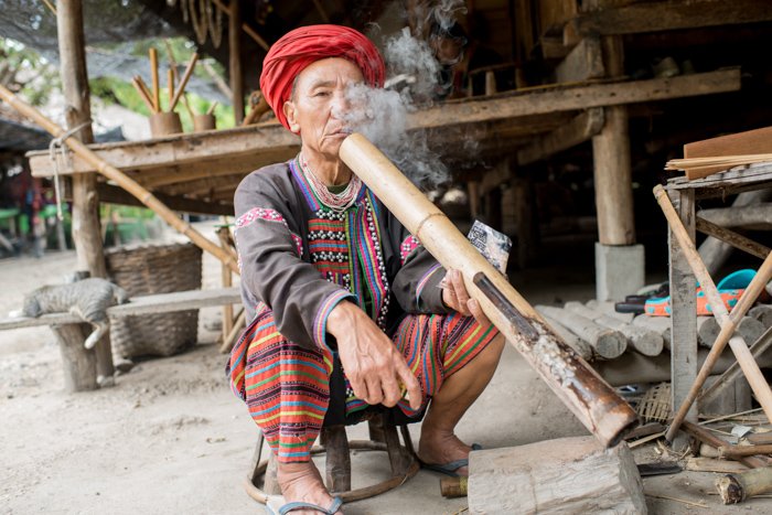 Экологический портрет мужчины лаху возле своего дома, курящего длинную бамбуковую трубку