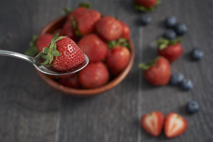 Full-frame sensor food-photography image of strawberries and blueberries with blurred table and background