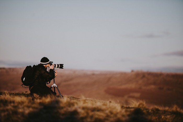 Фотограф снимает на открытом воздухе над коричневыми полями и серым скитом