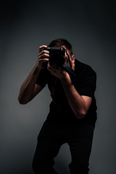 фотограф, стоящий перед камерой на темно-сером фоне