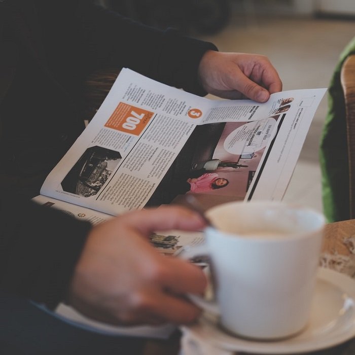 фотография человека, читающего местную газету, держа в руках чашку кофе