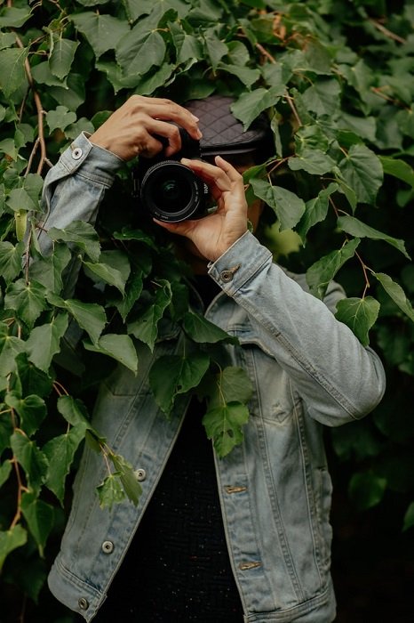 изображение фотографа, стоящего перед камерой под листьями