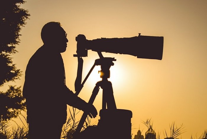 изображение мужчины, использующего телеобъектив на штативе с низким солнцем на заднем плане