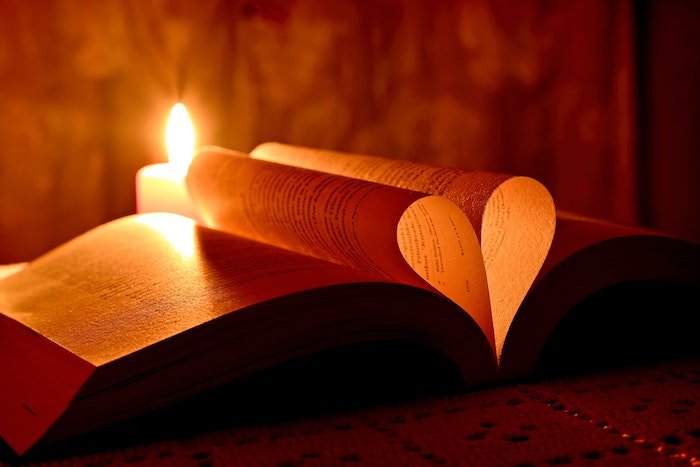 Книга со страницами, сложенными в форме сердца, подсвеченного зажженной свечой