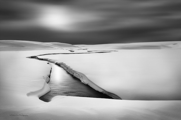 черно-белая пейзажная фотография: медленная река, текущая сквозь нетронутый снег