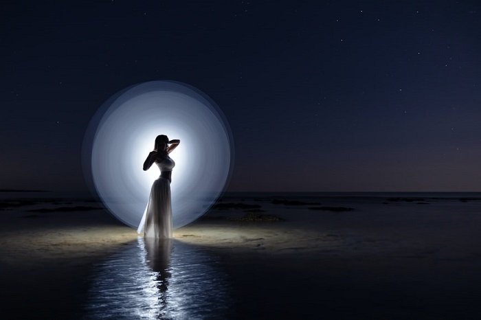 Ночная световая картина с белым светом, имитирующим луну позади женщины