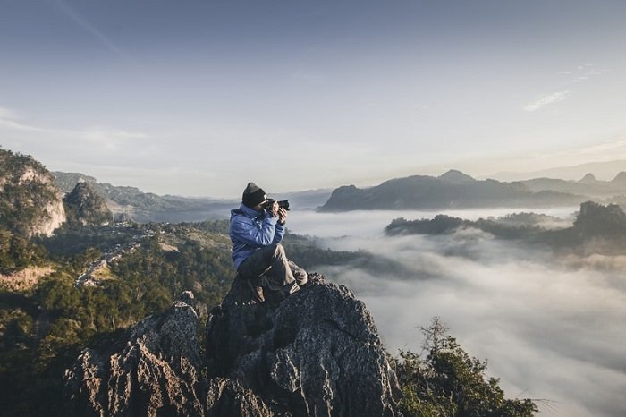 фотограф сидит на скале с горным пейзажем на заднем плане