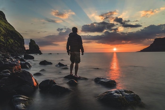 мужчина стоит на берегу моря на фоне заката