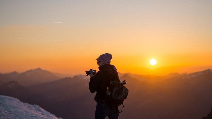 Фотограф в горной местности на фоне заката