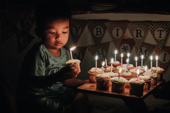 Ребенок держит кекс с зажженной свечой и поднос с кексами с зажженными свечами