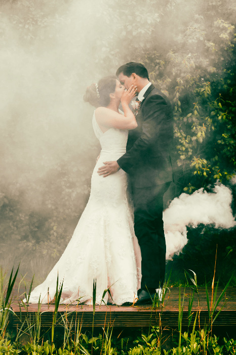 свадебная фотография пары, целующейся у озера, окруженного дымом