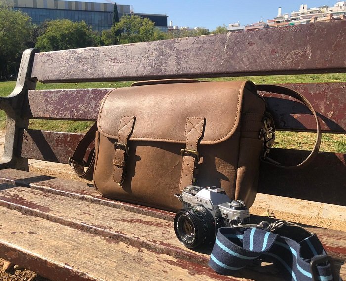 Кожаная сумка Black Forest позирует на скамейке с фотоаппаратом
