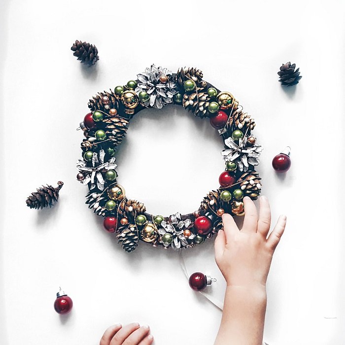 Christmas flat lay of the child's hand touching a pine cone wreath